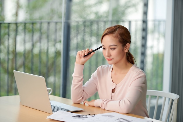 Jeune femme d'affaires écrivant dans un ordinateur portable tout en utilisant un ordinateur portable à table au bureau