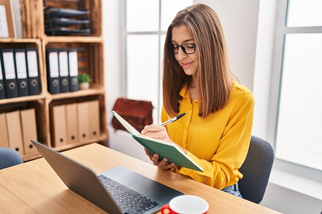 Jeune femme d'affaires écrivant sur un livre à l'aide d'un ordinateur portable travaillant au bureau