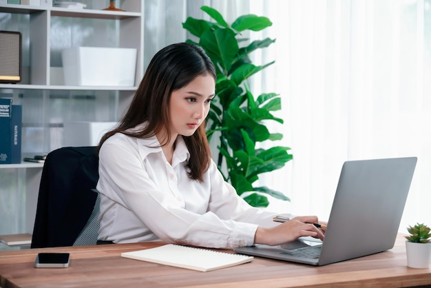 Jeune femme d'affaires enthousiaste asiatique au bureau moderne avec ordinateur portable