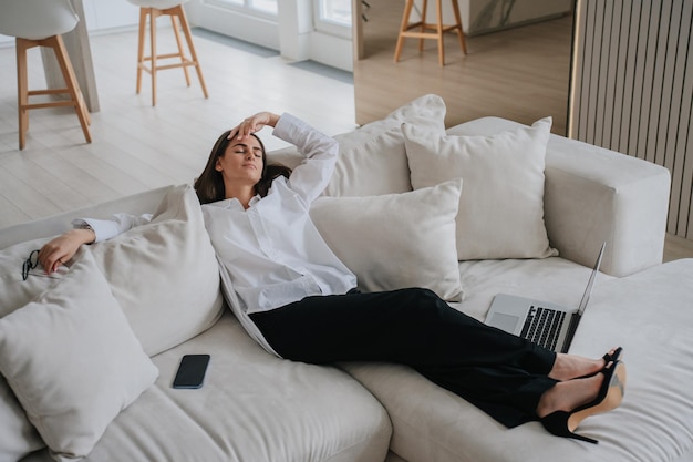 Photo jeune femme d'affaires épuisée allongée sur un canapé les yeux fermés après une journée de travail il y a un téléphone portable