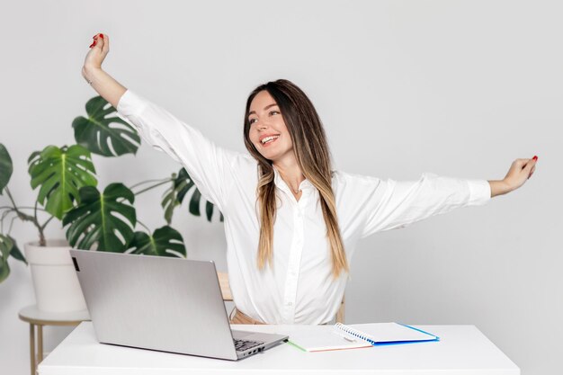 Une jeune femme d'affaires étend les bras assise à son bureau.