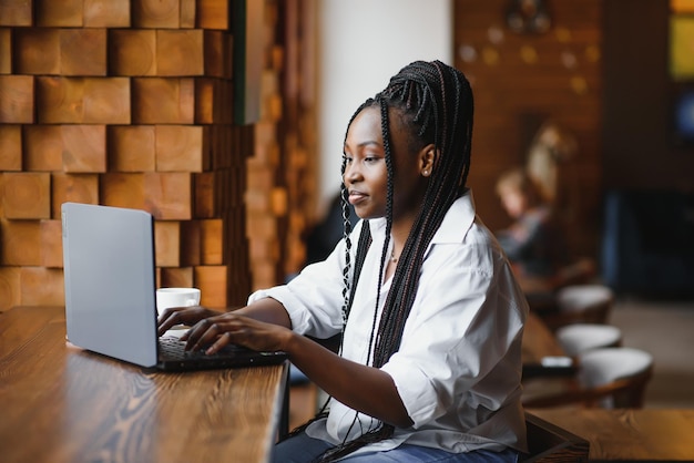 Jeune femme d'affaires ou étudiante afro-américaine concentrée regardant un ordinateur portable femme noire sérieuse travaillant ou étudiant avec un ordinateur faisant des recherches ou se préparant à un examen en ligne