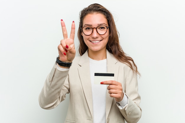 Jeune femme d'affaires européenne tenant une carte de crédit montrant le numéro deux avec les doigts.