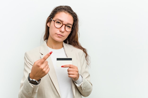 Jeune femme d'affaires européenne tenant une carte de crédit pointant du doigt vers vous comme si vous vous invitiez à vous rapprocher.