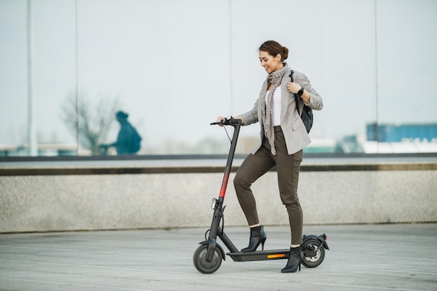 Une jeune femme d'affaires faisant du scooter électrique en se rendant au travail.