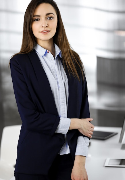 Une jeune femme d'affaires intelligente dans une veste bleue se tient sur son lieu de travail. Portrait d'un spécialiste dans un bureau moderne.