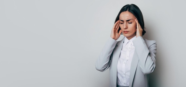 Jeune femme d'affaires isolée sur fond gris souffre de graves maux de tête désespérés et stressés parce que la douleur et la migraine après des troubles au travail