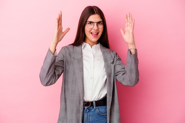 Jeune femme d'affaires isolée sur un mur rose recevant une agréable surprise, excitée et levant les mains