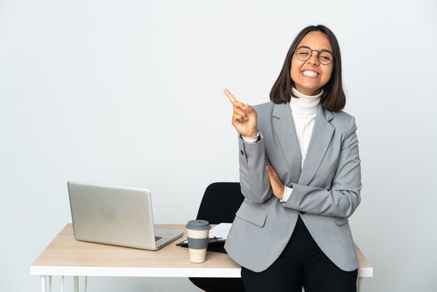 Jeune femme d'affaires latine travaillant dans un bureau isolé sur blanc montrant et levant un doigt en signe de la meilleure