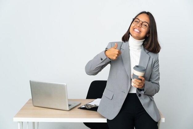 Jeune femme d'affaires latine travaillant dans un bureau isolé sur fond blanc donnant un geste du pouce vers le haut