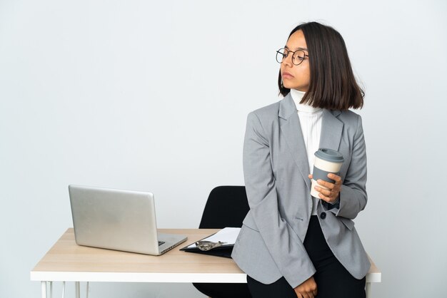 Jeune femme d'affaires latine travaillant dans un bureau isolé sur fond blanc regardant sur le côté