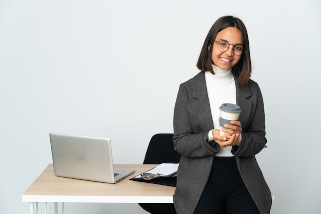 Jeune femme d'affaires latine travaillant dans un bureau isolé sur fond blanc en riant