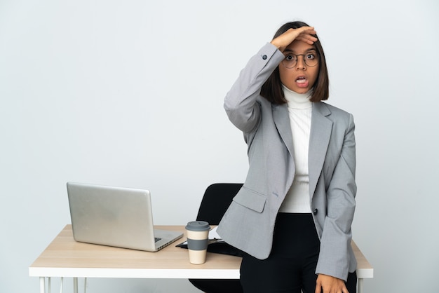 Jeune femme d'affaires latine travaillant dans un bureau isolé sur un mur blanc faisant un geste de surprise tout en regardant sur le côté