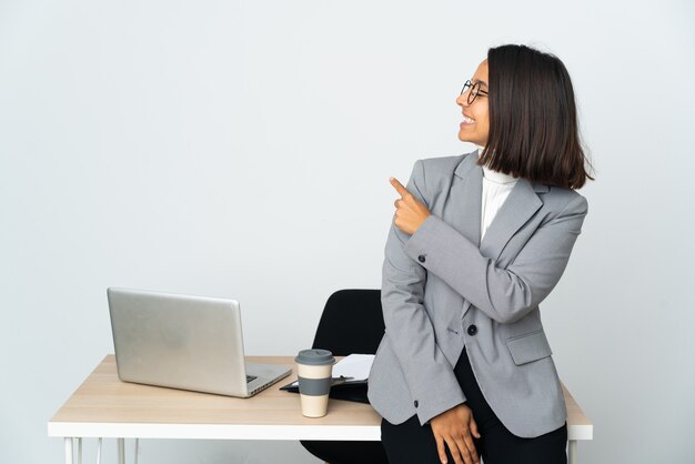 Jeune femme d'affaires latine travaillant dans un bureau isolé sur un mur blanc pointant vers l'arrière