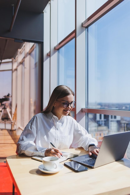 Jeune femme d'affaires à lunettes parle au téléphone dans le bureau Femme d'affaires envoyant des SMS au téléphone et travaillant sur un ordinateur portable