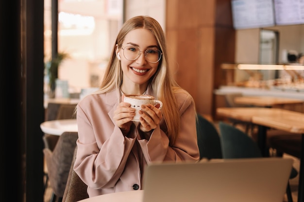 Une jeune femme d'affaires avec des lunettes parle au téléphone et travaille en ligne à l'aide d'un ordinateur portable dans un café