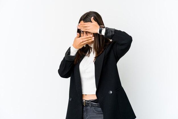 Jeune femme d'affaires métisse isolée sur un mur blanc clignote à travers les doigts, visage couvrant embarrassé.