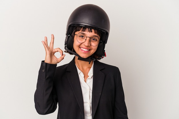 Jeune femme d'affaires métisse portant un casque de moto isolé joyeux et confiant montrant un geste correct.