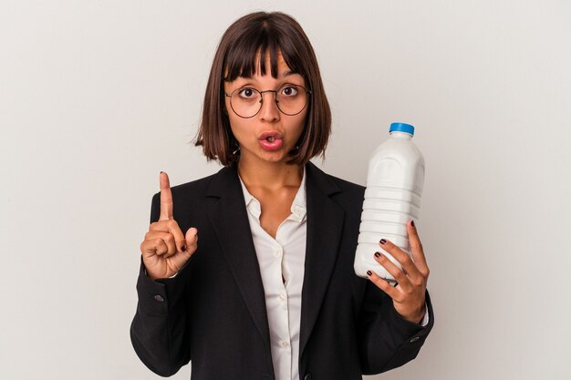 Jeune femme d'affaires métisse tenant une bouteille de lait isolée sur fond blanc ayant une bonne idée, concept de créativité.