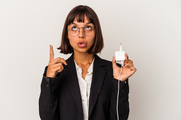 Jeune femme d'affaires métisse tenant un chargeur de téléphone isolé sur fond blanc personne pointant à la main vers un espace de copie de chemise, fière et confiante
