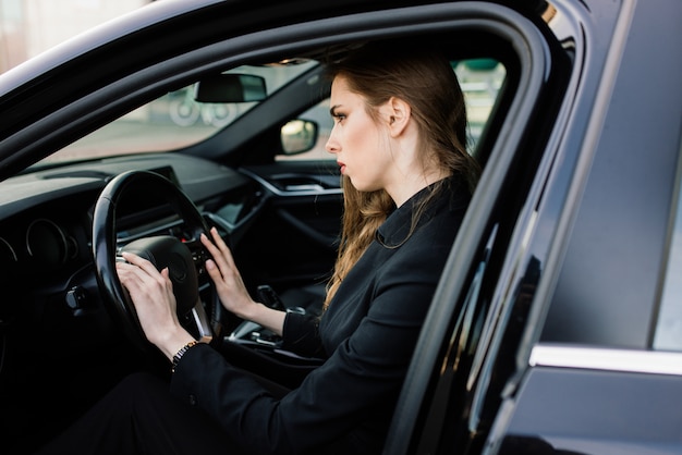 Jeune femme d'affaires en noir avec une voiture chère