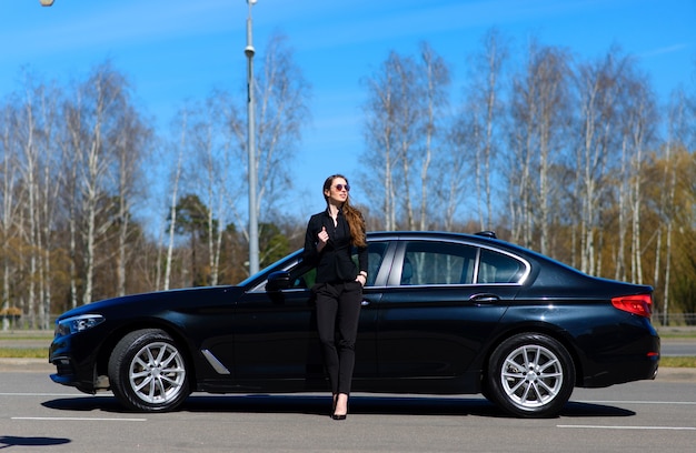 Jeune femme d'affaires en noir avec une voiture chère