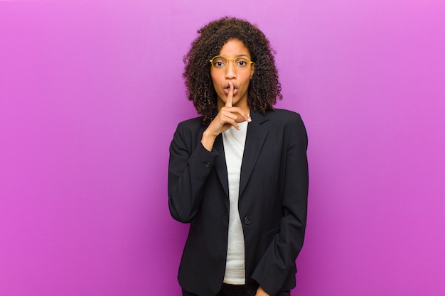 Jeune femme d'affaires noire demandant le silence et le calme, faisant des gestes avec le doigt devant la bouche, disant chut ou gardant un secret