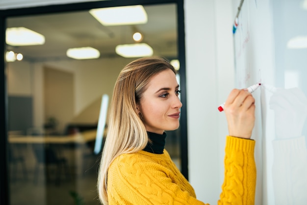 Jeune femme d&#39;affaires occasionnel travaillant contre le tableau blanc.