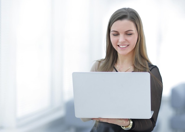 Jeune femme d'affaires avec ordinateur portable debout dans le hall du bureau