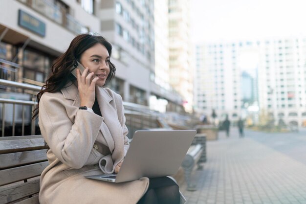 Jeune femme d'affaires parlant au téléphone mobile travaillant sur un ordinateur portable en ligne à l'extérieur du bureau