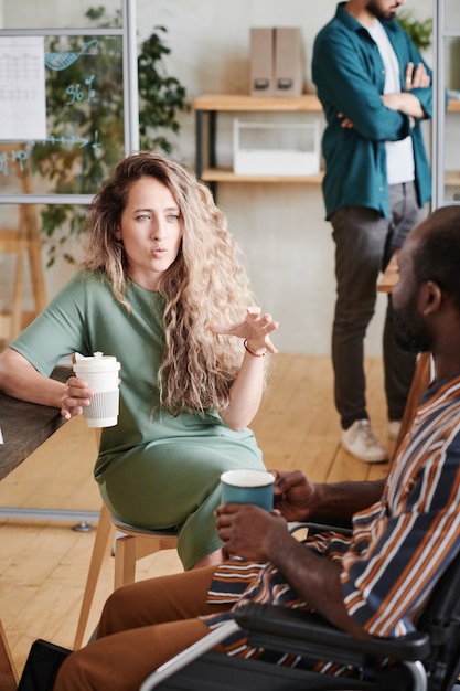 Jeune femme d'affaires parlant à son collègue pendant qu'ils boivent du café ensemble au bureau