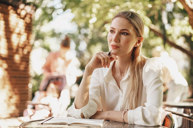 Jeune femme d'affaires pensive assise dans un café en plein air et prenant des notes