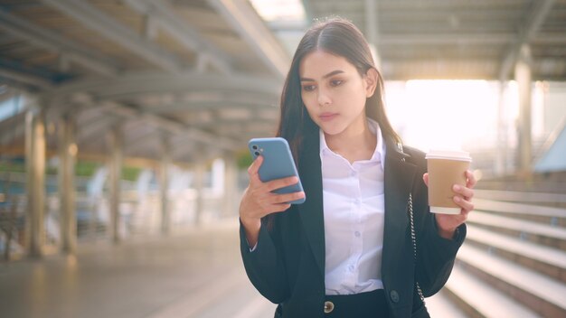 Une jeune femme d'affaires portant un costume noir utilise un téléphone intelligent