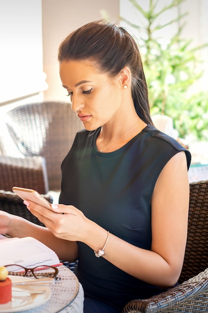 Jeune femme d'affaires prend des notes dans le cahier du smartphone en le regardant travailler dans le café