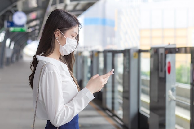 Jeune femme d'affaires professionnelle asiatique se tient sur une station de train aérien en ville portant un masque facial