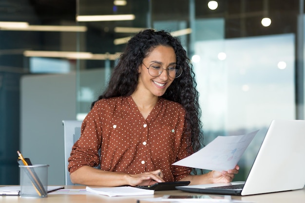 Jeune femme d'affaires prospère derrière la paperasse femme hispanique travaillant avec des documents et des contrats