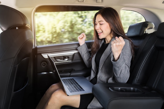 Jeune femme d'affaires prospère utilisant un ordinateur portable alors qu'elle était assise sur le siège arrière de la voiture