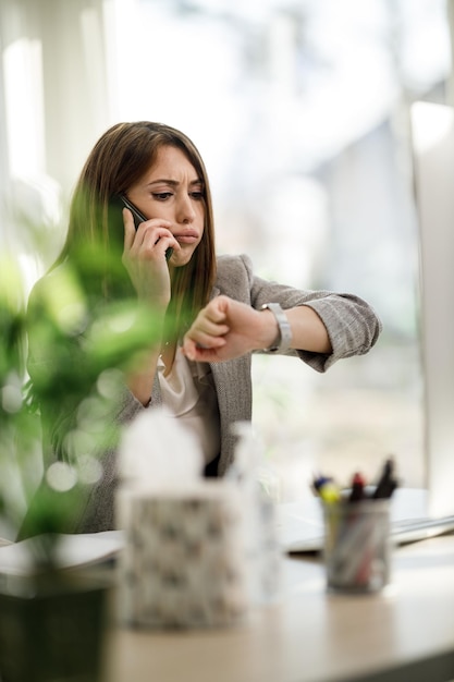 Une jeune femme d'affaires qui a l'air stressée tout en parlant sur un smartphone dans son bureau à domicile.