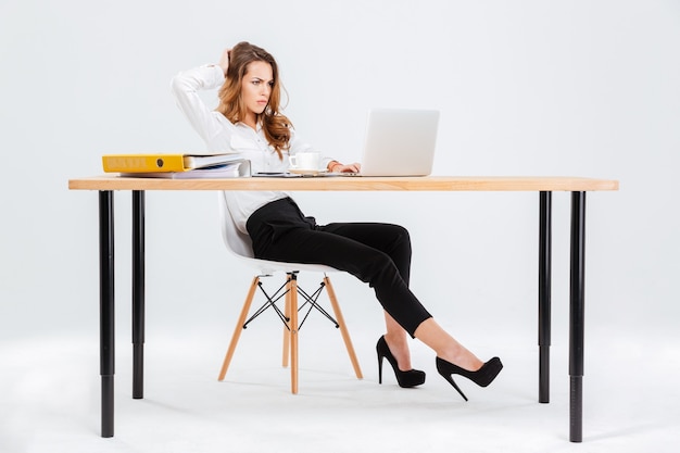 Jeune femme d'affaires réfléchie pensant et travaillant avec un ordinateur portable sur fond blanc