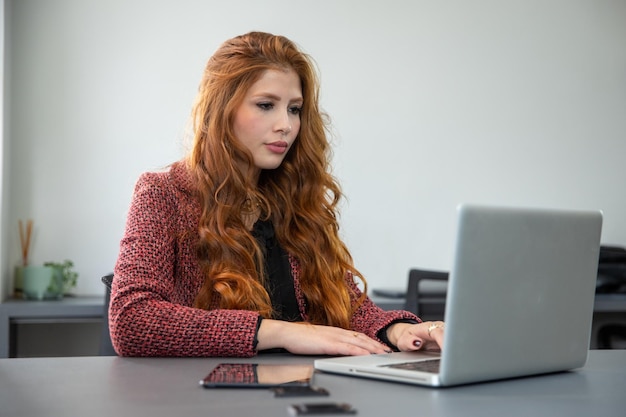 jeune femme d'affaires rousse assise devant un ordinateur regardant la caméra