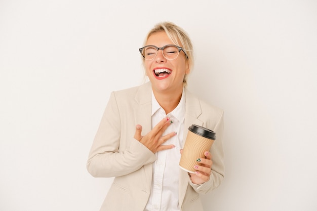 Jeune femme d'affaires russe tenant du café à emporter isolé sur fond blanc éclate de rire en gardant la main sur la poitrine.