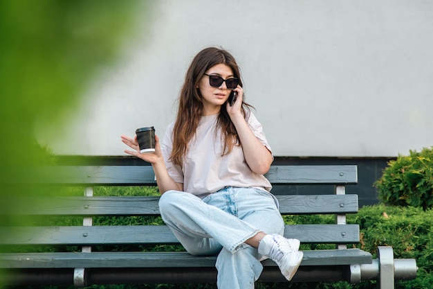 La jeune femme d'affaires s'assied sur un banc et parle au téléphone