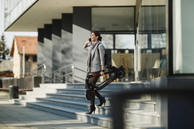 Une jeune femme d'affaires avec un scooter électrique à l'aide d'un smartphone.