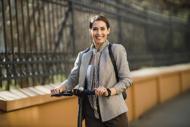 Une jeune femme d'affaires avec un scooter électrique va travailler. Regarder la caméra.