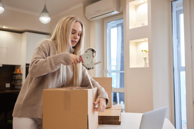 Jeune femme d'affaires scotchant une boîte en carton dans le déménagement du bureau et le nouveau concept d'entreprise