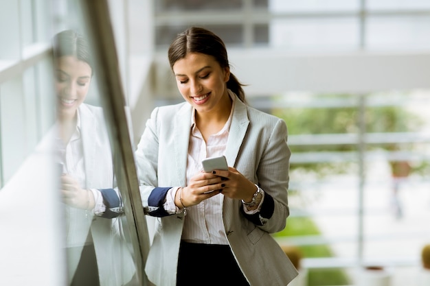 Jeune femme d&#39;affaires se dresse sur les escaliers au bureau et utilise un téléphone mobile