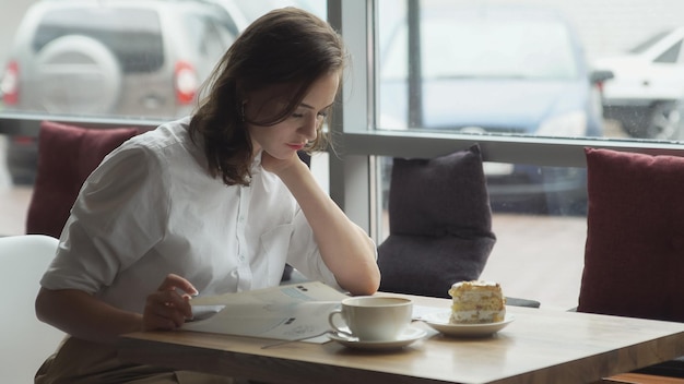 Une jeune femme d'affaires se repose pendant une pause déjeuner dans un café et feuillette un magazine de mode pour femmes