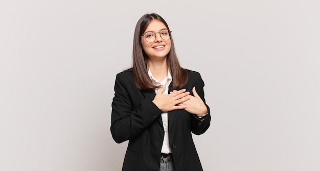 Jeune femme d'affaires se sentant romantique, heureuse et amoureuse, souriant joyeusement et se tenant la main près du cœur