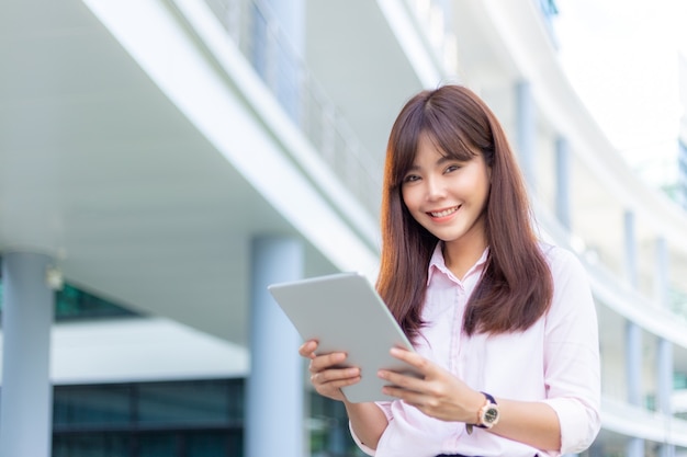 Jeune femme d'affaires séduisante dans sa chemise rose utilisant sa tablette pour vérifier les médias sociaux