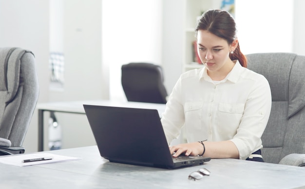 Jeune femme d'affaires séduisante travaillant au bureau souriant à la recherche d'un ordinateur portable.